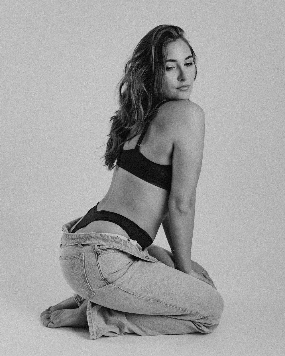 Black and white photo of a woman in denim and black top posing on her knees.