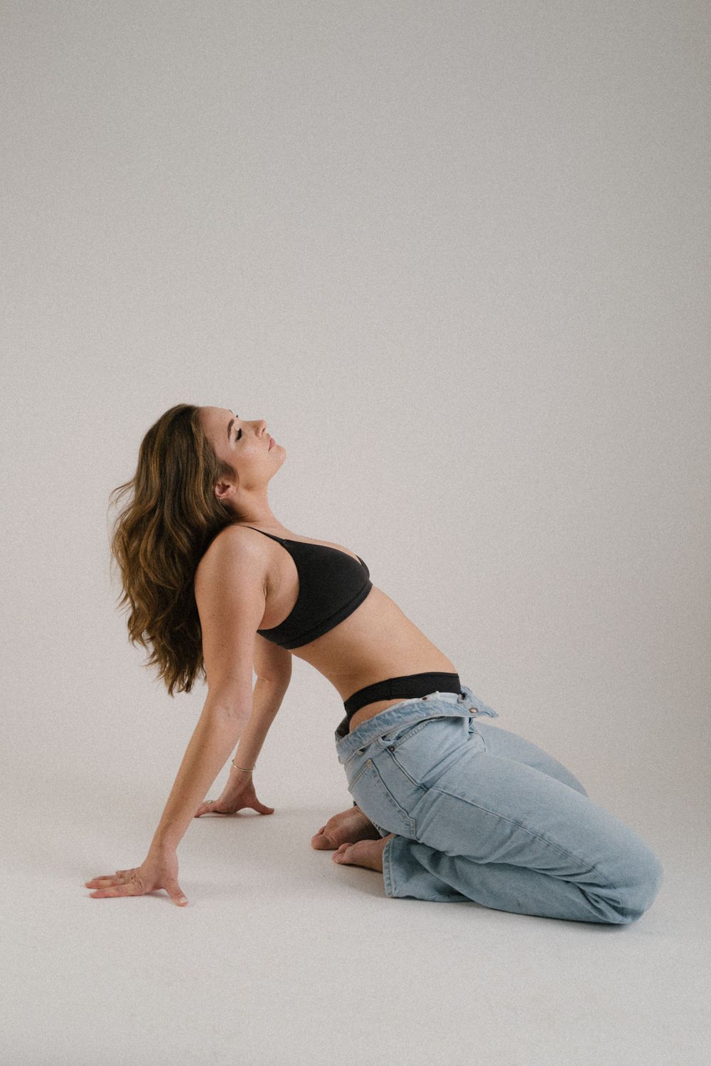 Woman in casual wear performs artistic pose during studio photoshoot.