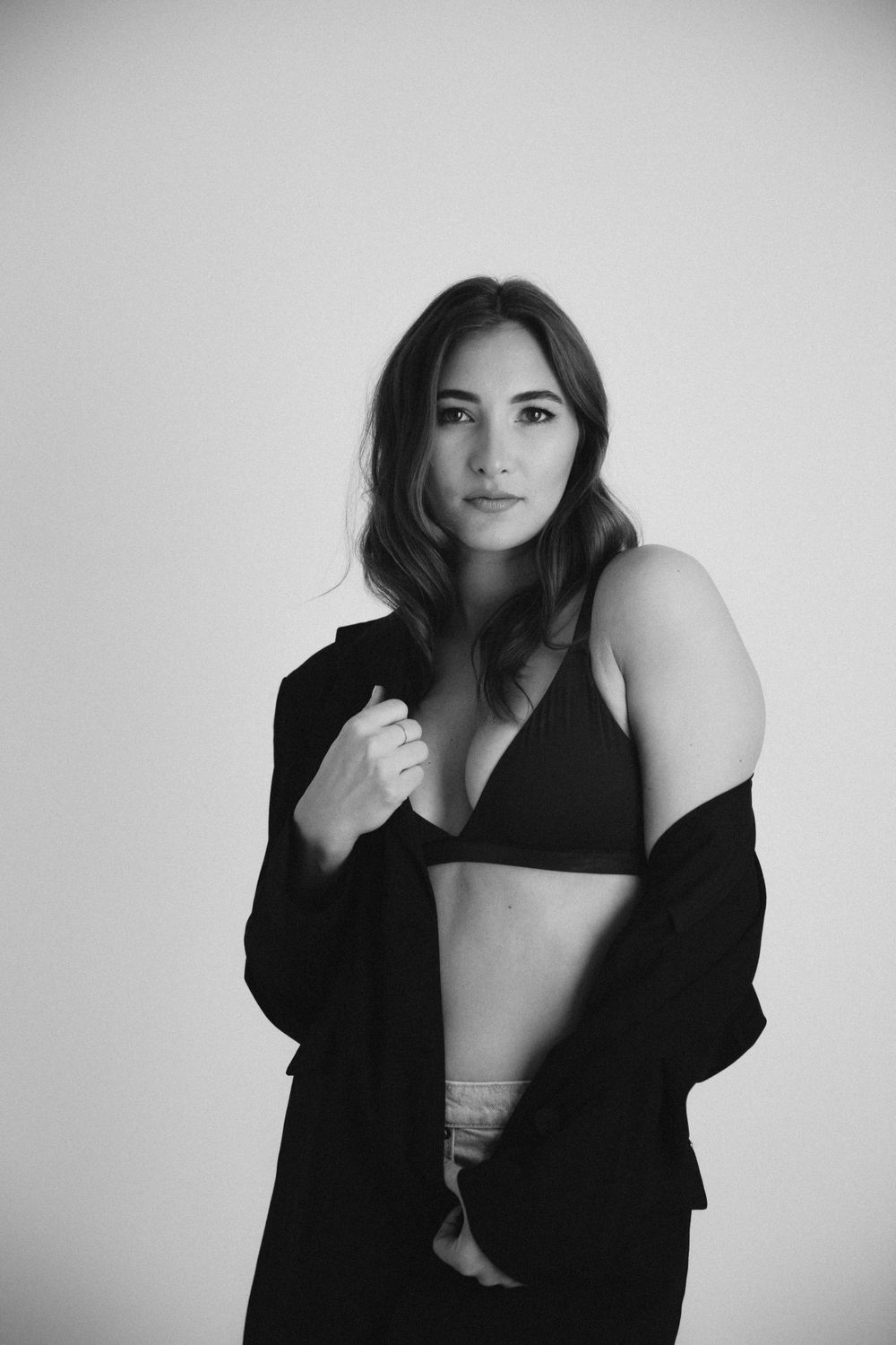 Intimate portrait session with black jacket and bralette against white background.