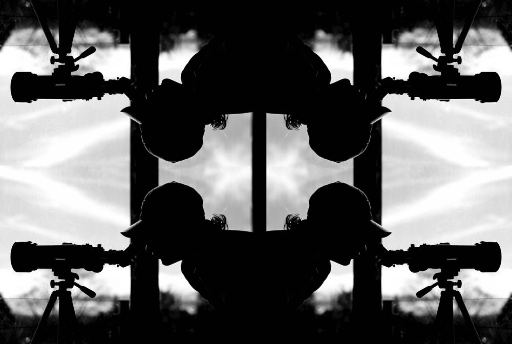 An art shot that is a black and white mirror image of a teen boy looking through a telescope.