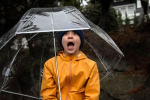 Boy in a yellow rain coat makes an animated facial expression while holding an umbrella in West Seattle.