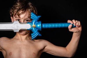 Boy poses with a toy Zelda sword in front of his face standing in front of a black backdrop.