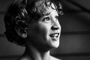 Black and white image of a boy smiling with curly hair.
