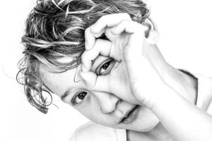 Black and white image of a boy who is making a circle with his fingers and peeks through to look at the camera.