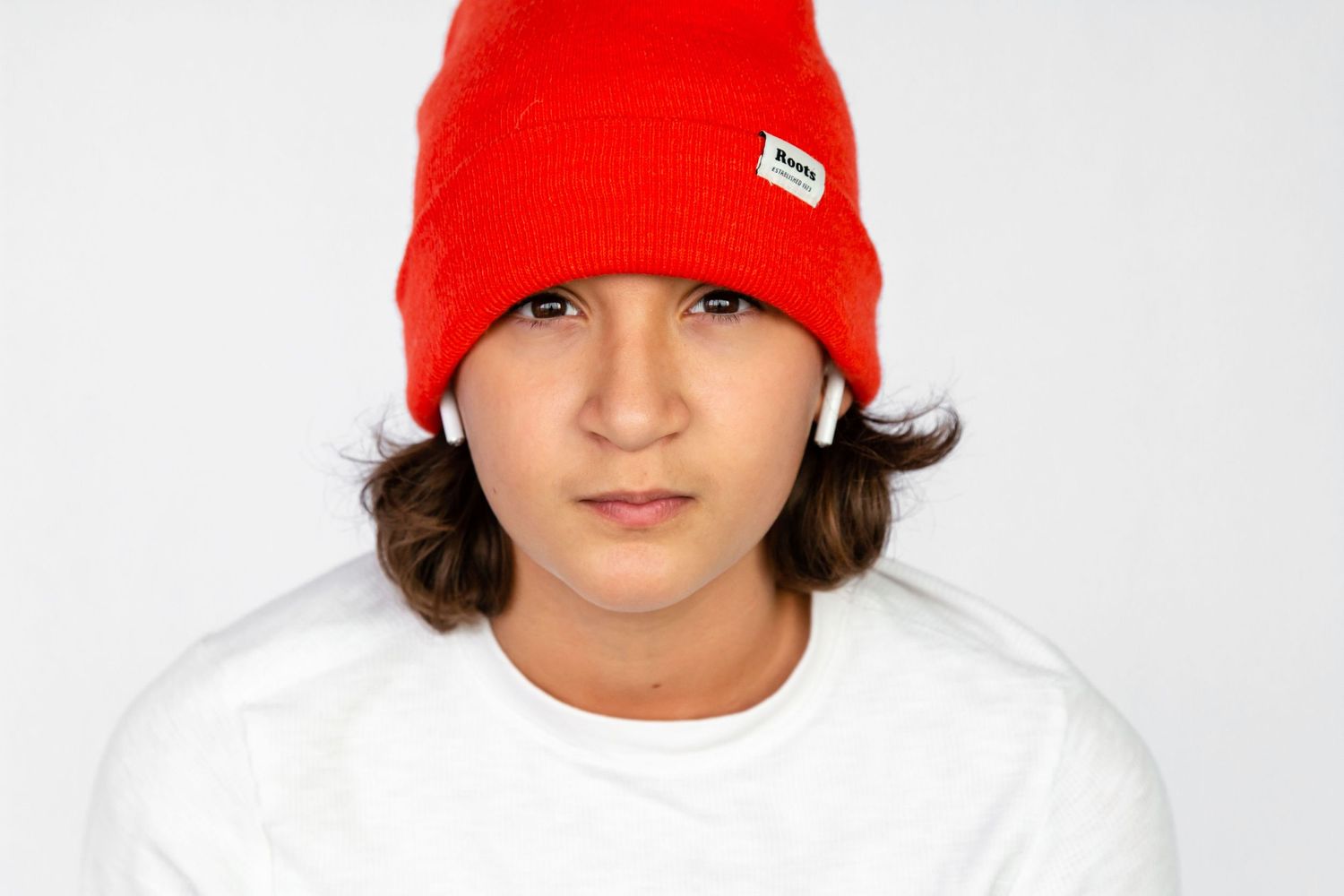 Casual headshot of a teen boy wearing air pods and an orange beanie hat in front of a white backdrop.