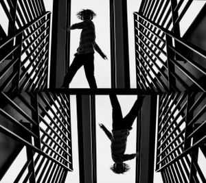 Black and white mirror image of a boy dancing at the top of a modern metal staircase in his home.
