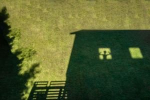 Silhouette and shadow of a boy looking out to the backyard grass while in a house during the pandemic.