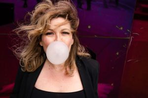 Woman blowing a large bubble with pink bubblegum, leaning against a magenta wall at the MoPop Museum at Seattle Center