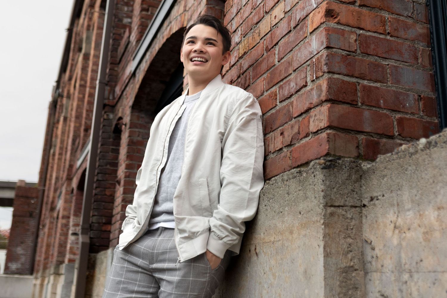 A graduating senior smiles as he leans on a brick wall during a Senior photo shoot in Georgetown Seattle.