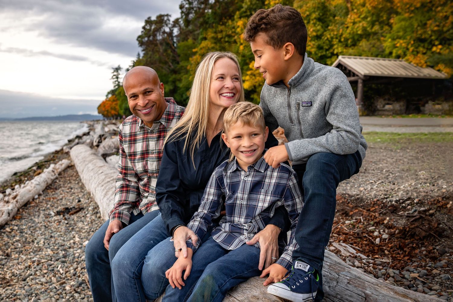 Family of four, posing on driftwood for a family session in Lincoln Park Seattle at the beach.