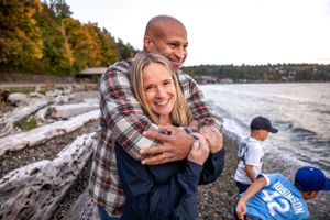 Couple hugging with smiles as they look out toward the sunset in West Seattle at Lincoln Park.