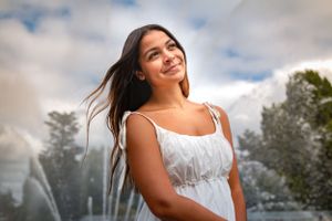 A teenage graduating senior girl looks up to the sky with the Seattle Center fountain spraying in the background.