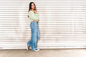 Girl stands in front of a metal garage wall in jeans and green top, during a Senior session at Seattle Center