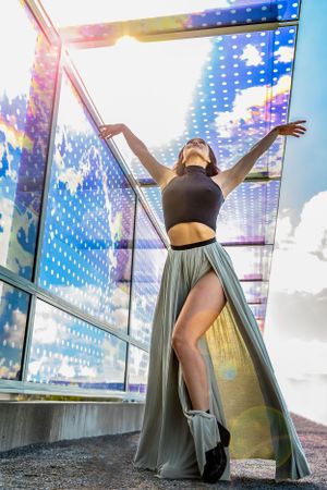 Dancer in a long skirt, stands under a glass, multi-colored walkway on a fall morning at the Sculpture Park Seattle.