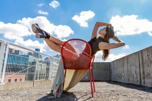 Dancer sits & poses in a red chair with blue sky and puffy white clouds in the background at the Sculpture Park Seattle.