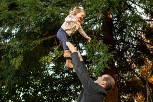 A dad throws his daughter into the air surrounded by trees during a family photo session in Olympia Washington.