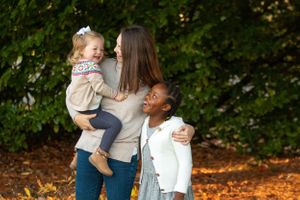 Front yard photo of a mom and her two smiling daughters in front of a tree in Olympia, Washington.