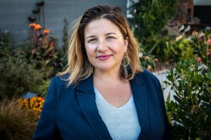 Headshot of woman in her backyard wearing a blazer with flowers in the background.