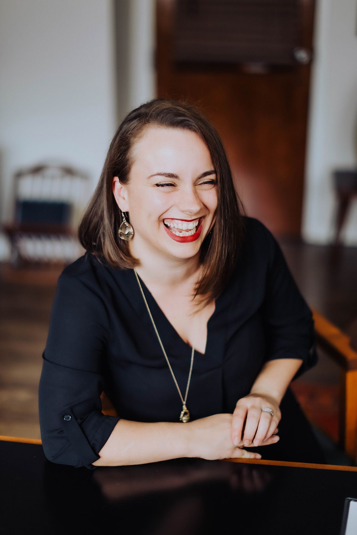 A candid portrait of someone laughing while seated at a dark table.