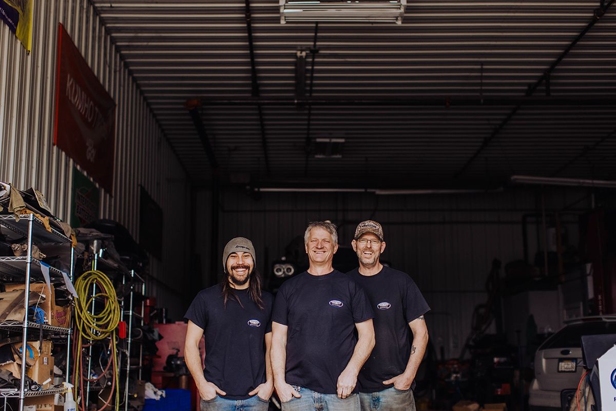 Three workers in navy uniforms standing together in an industrial warehouse setting.