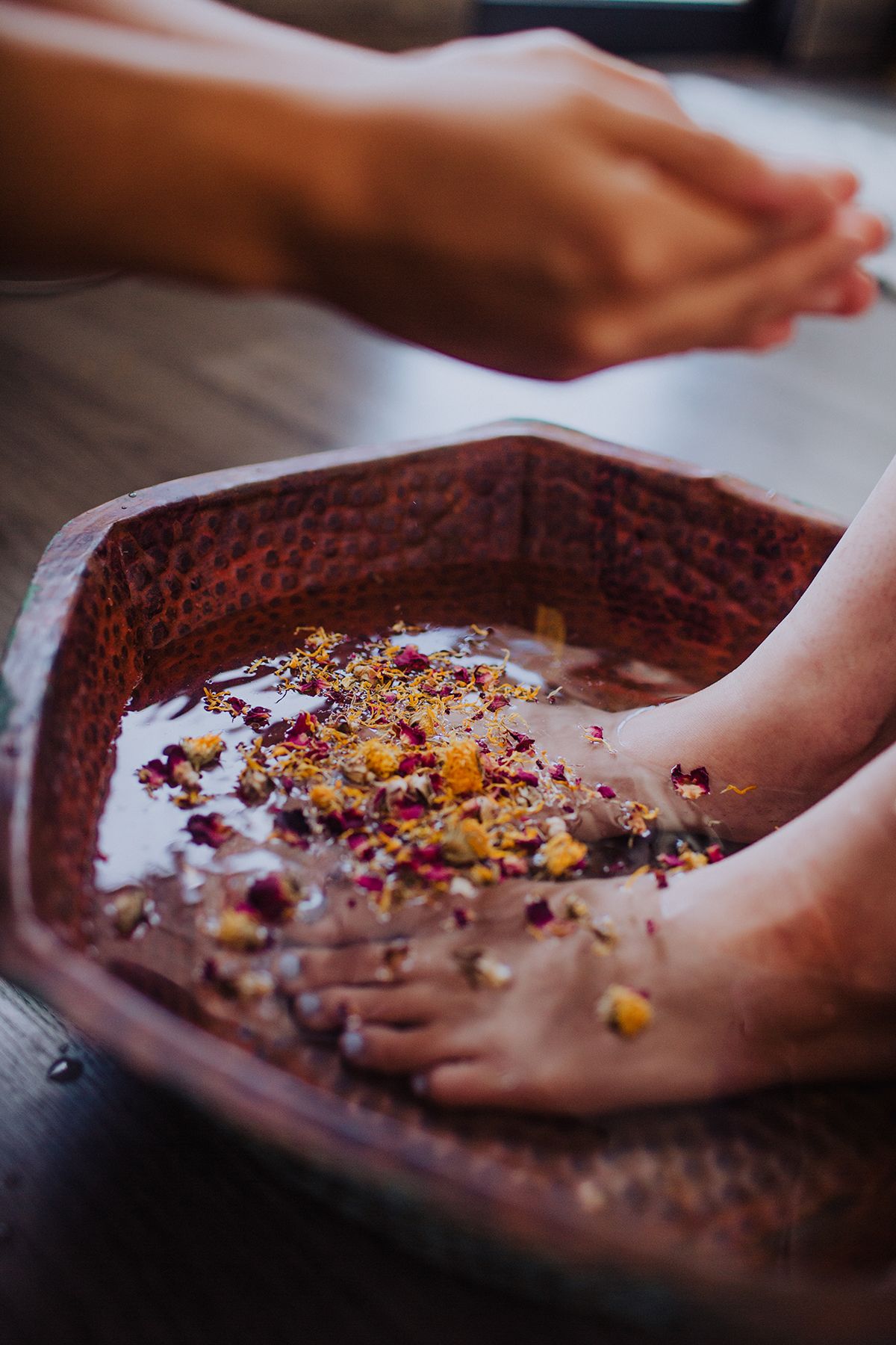 Hands performing a spa treatment with flower petals in a wooden bowl filled with water.