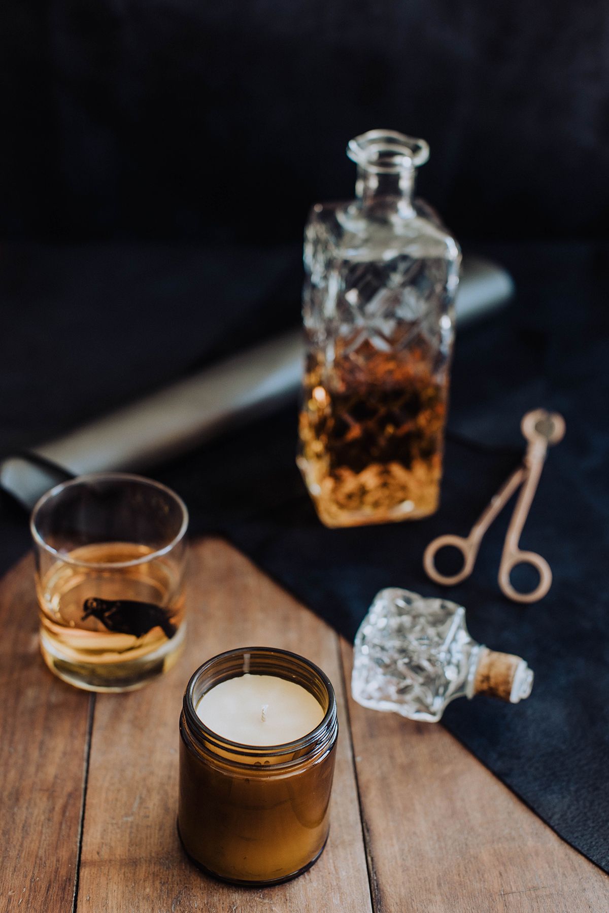Whiskey glass and decanter with ice tongs on dark wooden surface.