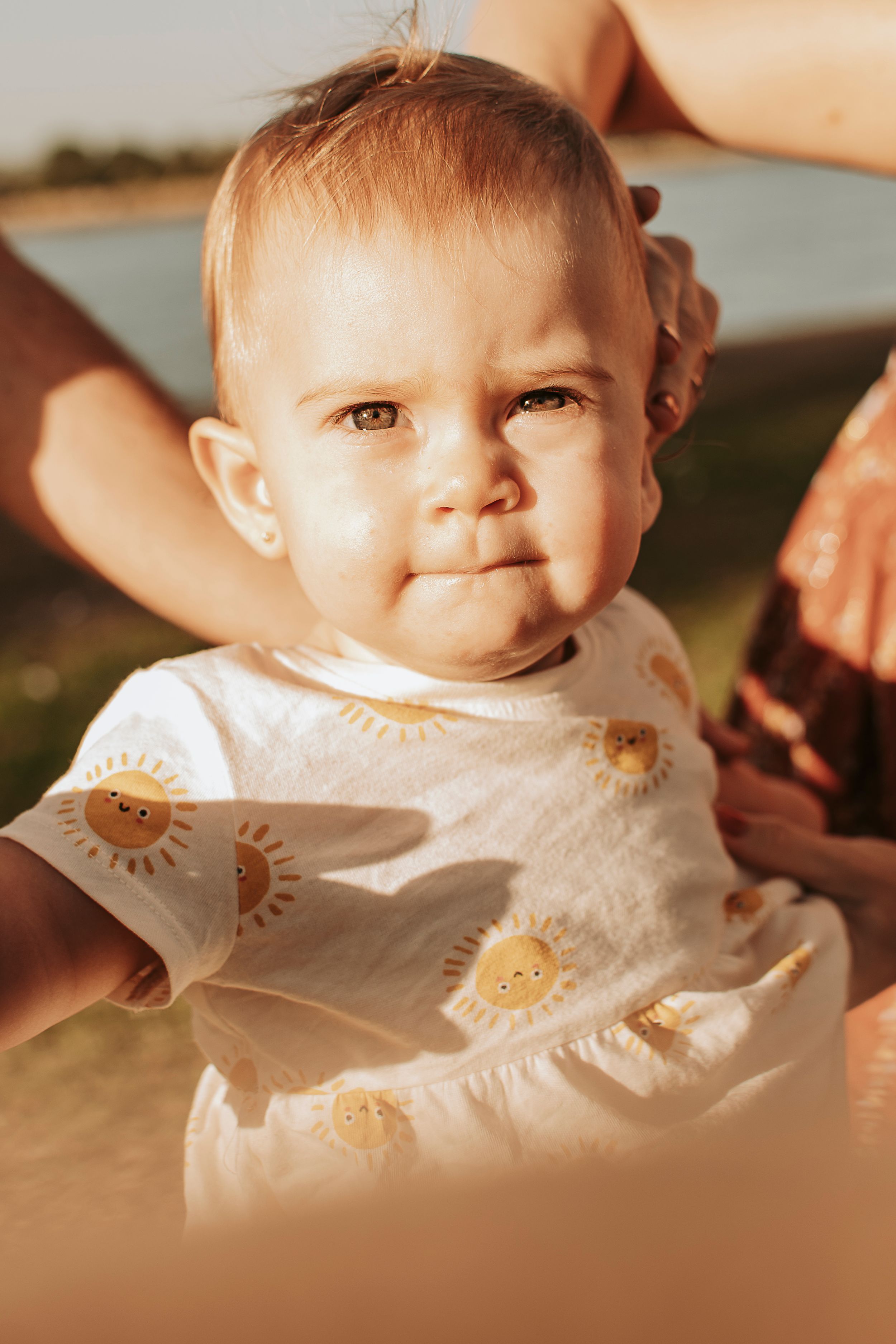 Close-up photos showcase a baby wearing a white outfit with sun designs in warm lighting.
