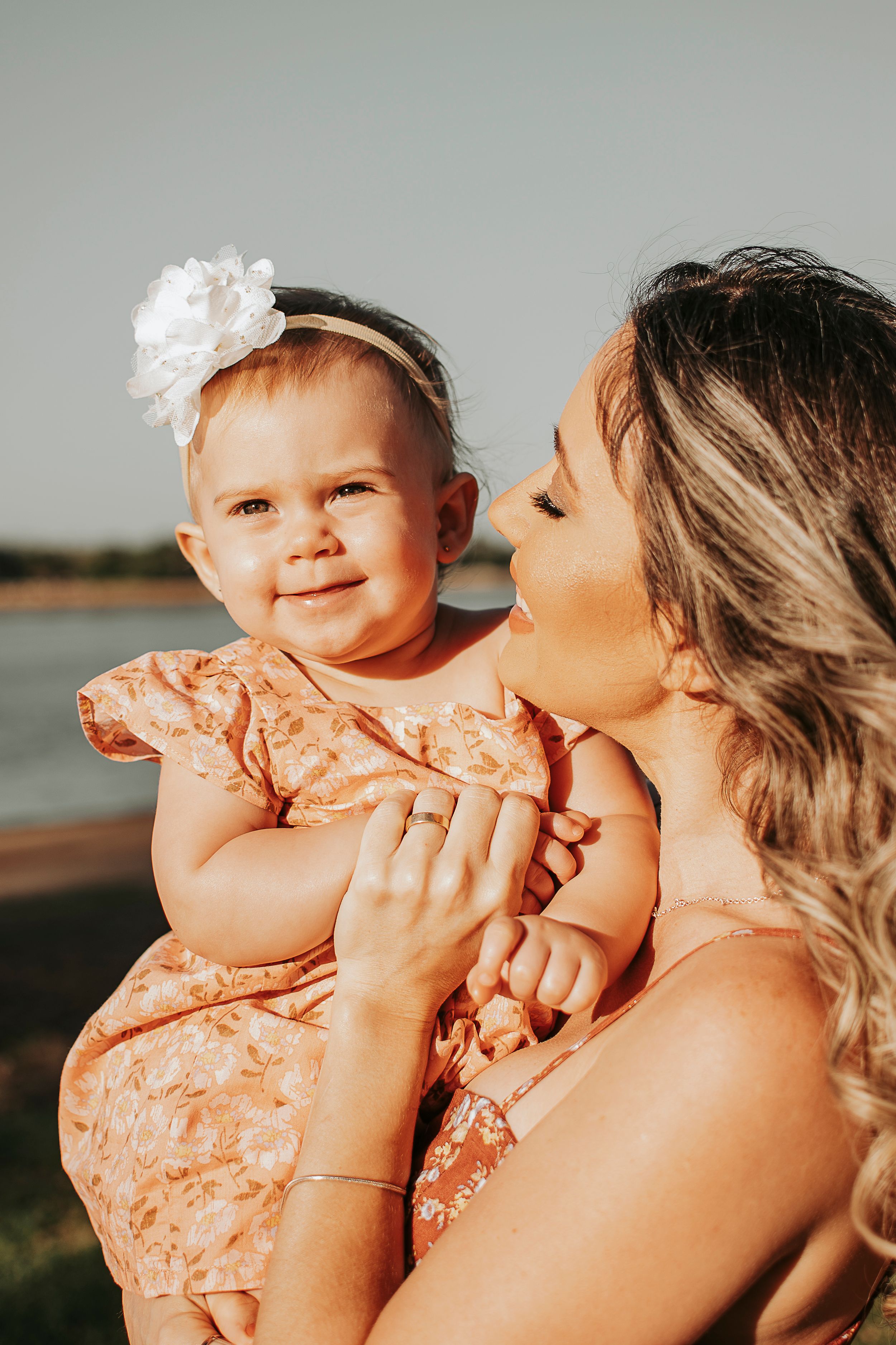 A tender moment between parent and baby in peachy sunset light at a waterfront location.