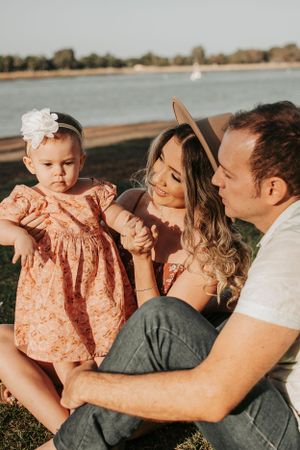 A joyful outdoor family photoshoot with a baby wearing a peach dress near the water.