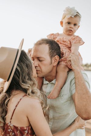 An intimate family portrait during golden hour with a baby perched on shoulders.