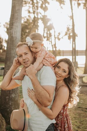 A happy family portrait outdoors with palm trees and sunset lighting in the background.
