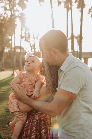 Sweet family moment captured during sunset with trees in background.