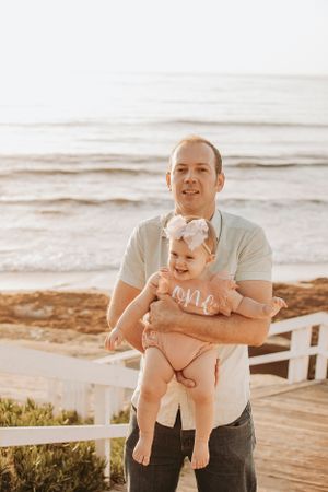 Parent and baby share joyful moment together on sunny beach boardwalk.