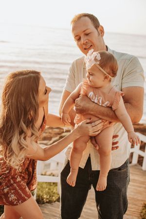 Family plays together and shares kisses with baby on beach at sunset.