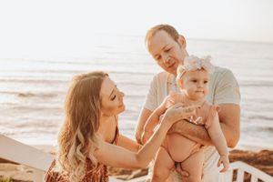 Family shares playful moments with baby on coastal boardwalk during golden hour.