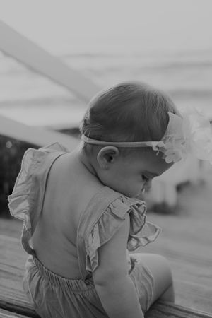 Black and white close-up of baby wearing ruffled dress outdoors.