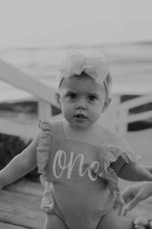 Baby wearing pink ruffled romper with 'one' text in black and white photo series.