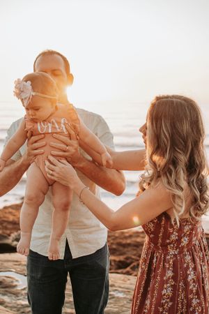 Family playing together on rocky beach during golden hour.