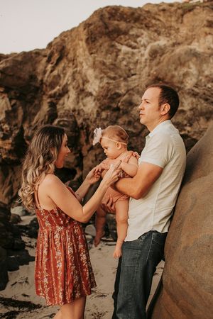 A family shares a tender moment against a rocky coastal backdrop during sunset.