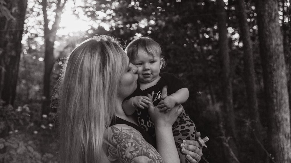Black and white photo of tender moment between parent and child in forest setting.