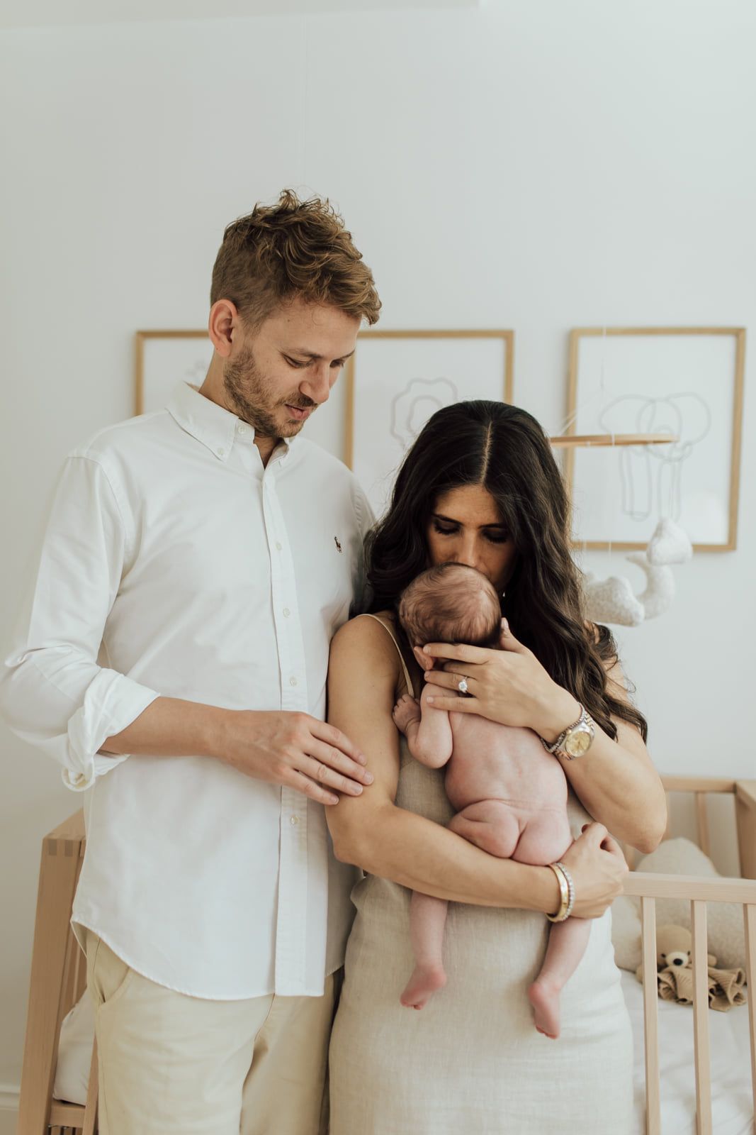 Parents in white and linen outfits lovingly gazing at newborn in nursery.