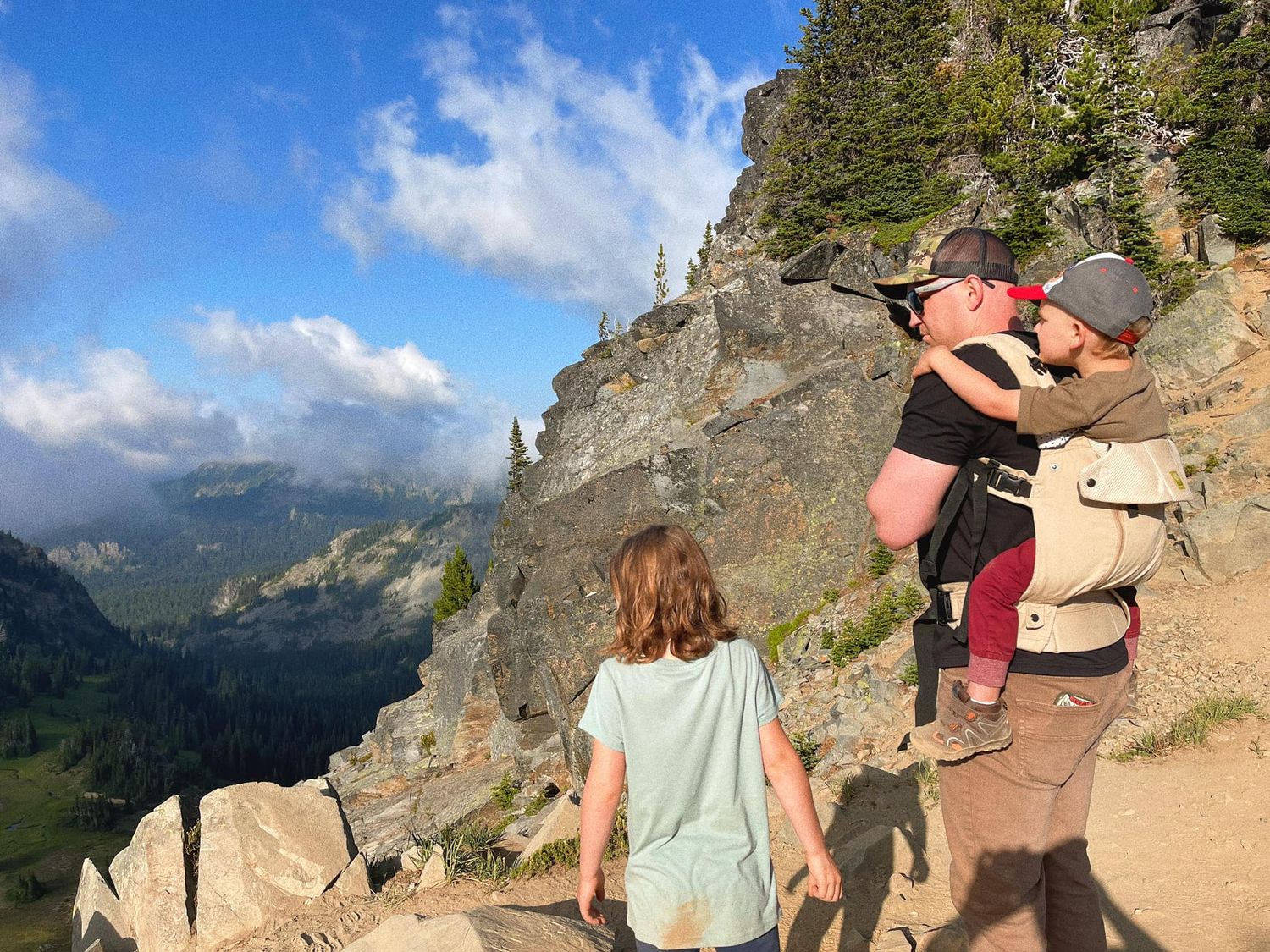 Hikers on a mountain trail pause to take photos of the scenic alpine valley in Mt. Rainier National Park on a sunny summer day.