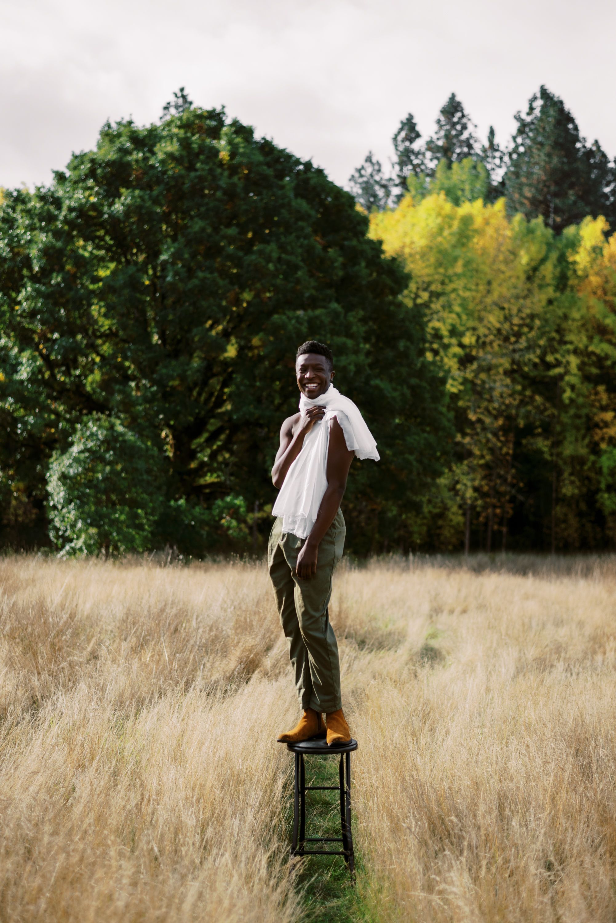 Person stands confidently on green stool in meadow with autumn trees in background.