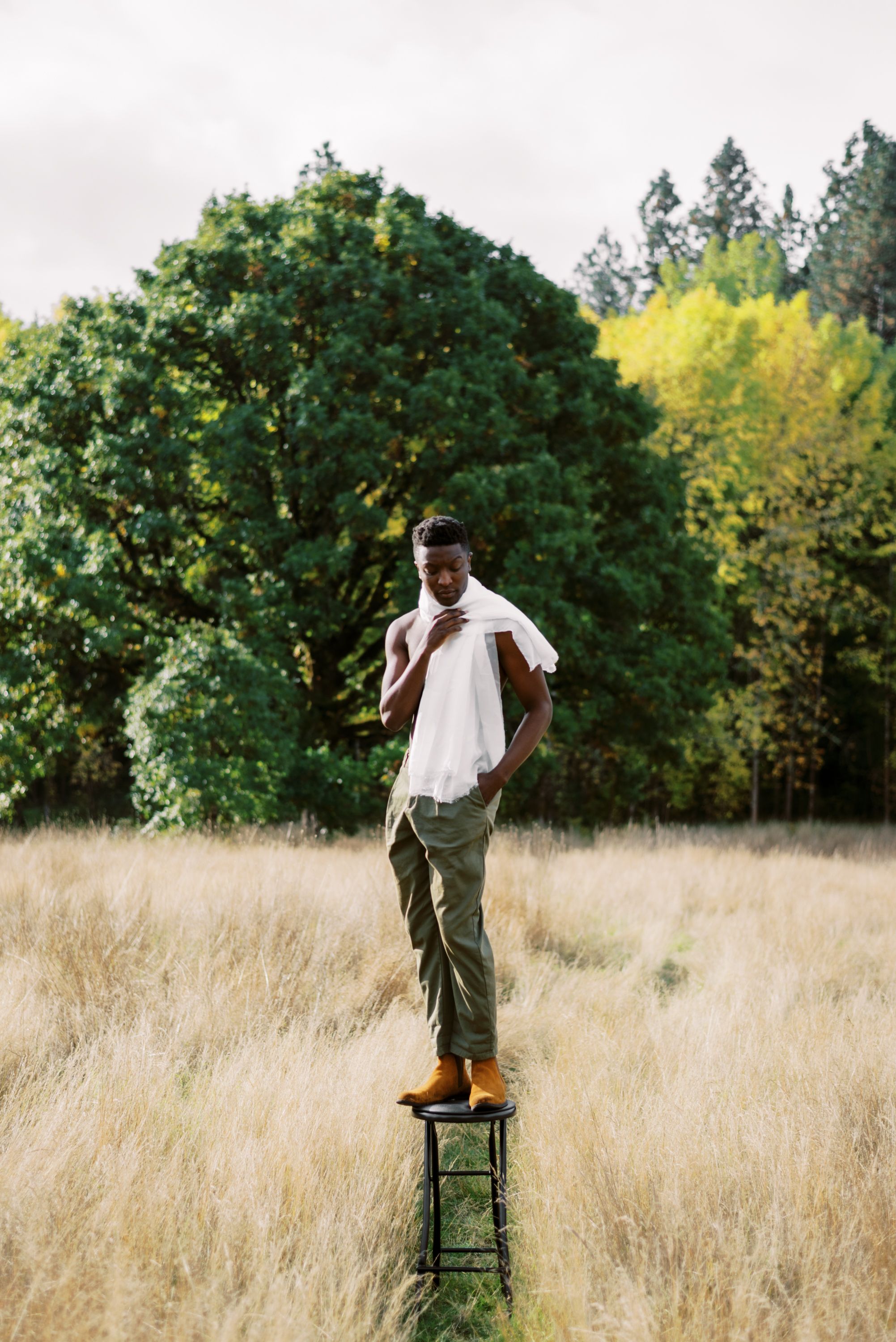 Figure in white shirt balances on vintage stool amid golden grass field.