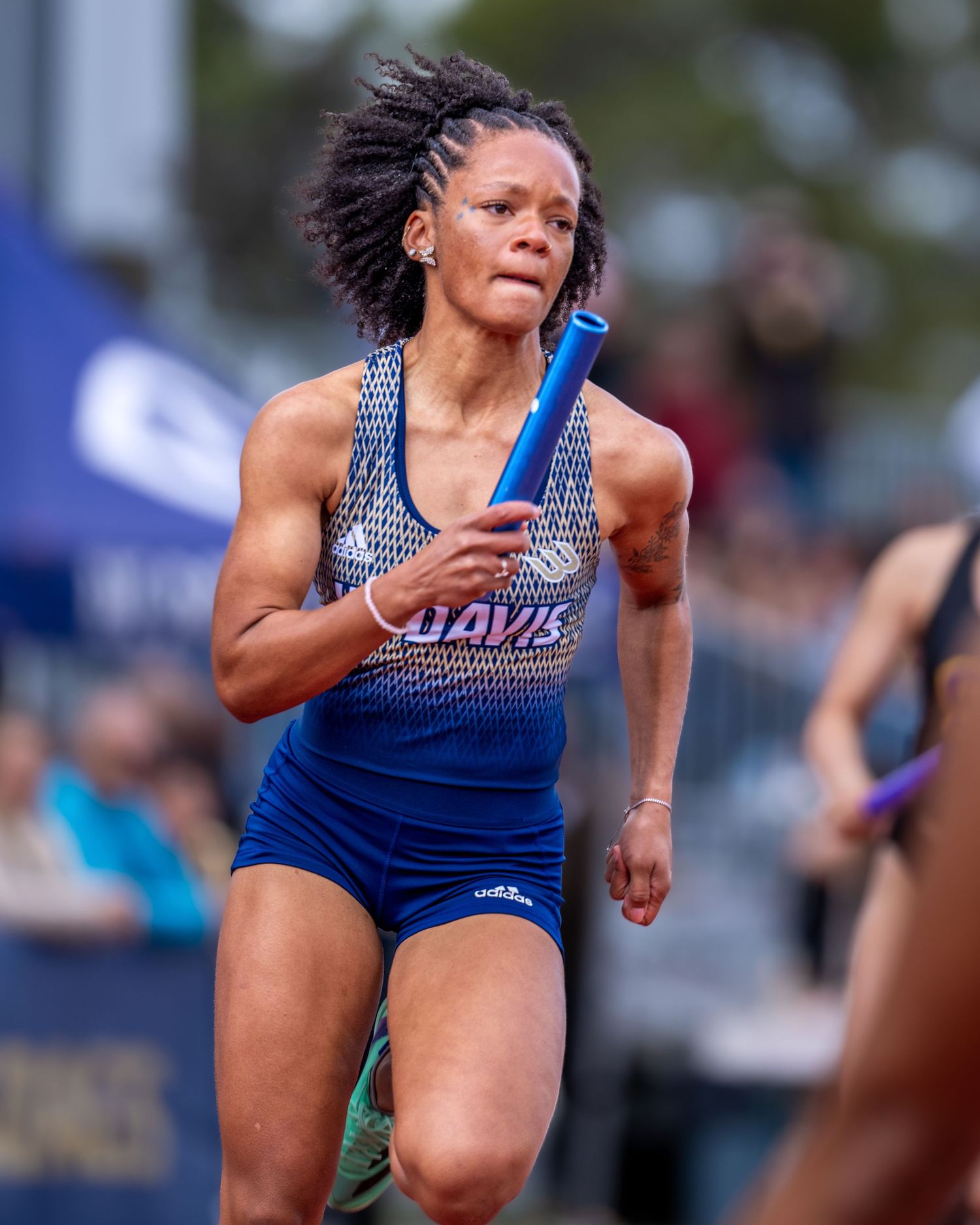 Track athlete in blue uniform competing in relay race with baton.