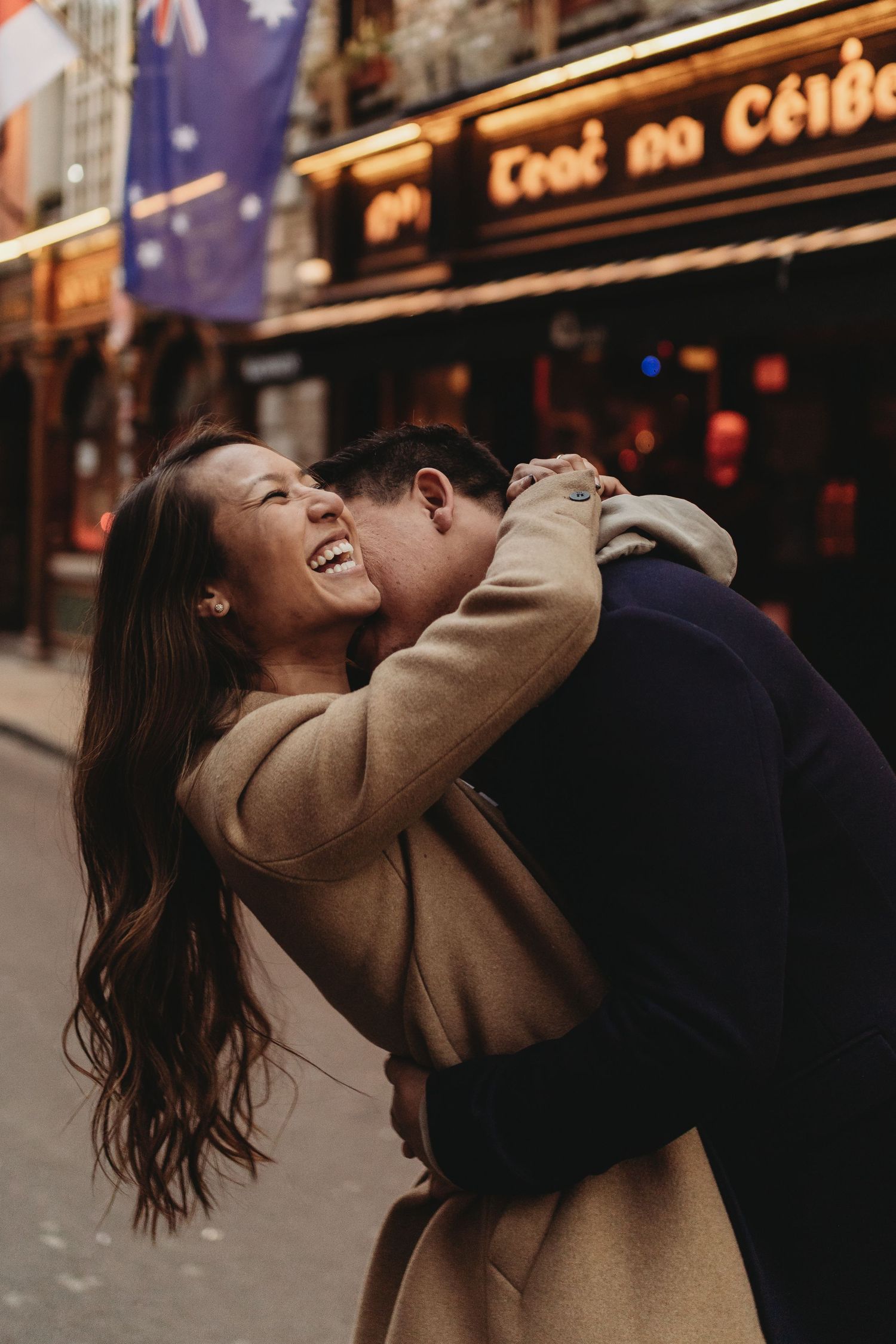 Joyful couple sharing a romantic moment outside an Irish pub with flags visible.