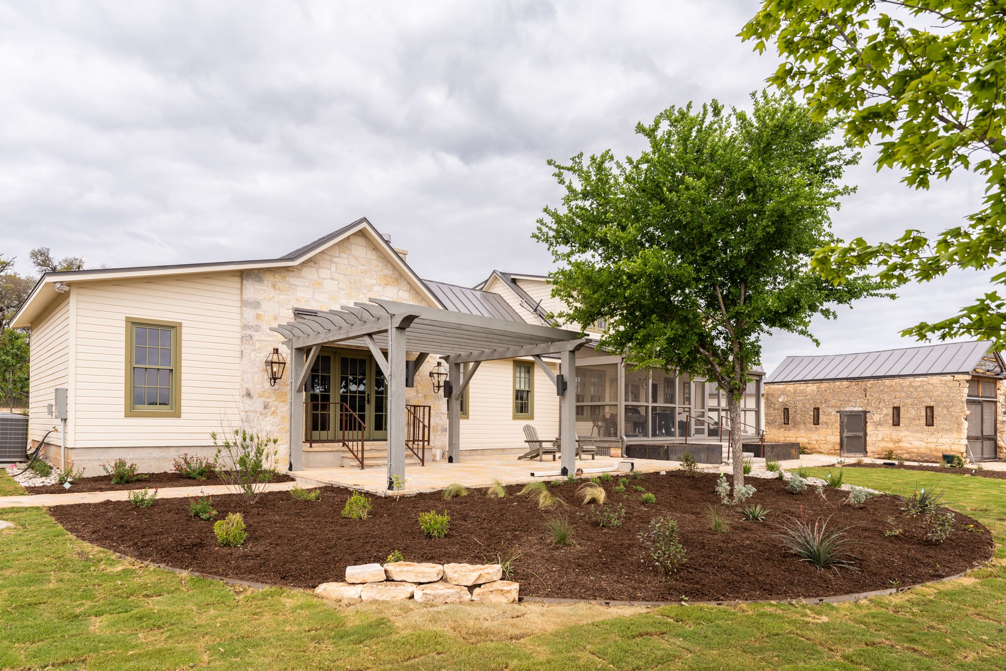 Modern farmhouse style home with cream exterior, arched entrance and fresh landscaping with mulch beds on a green lawn.