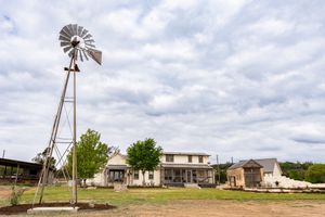 A series of old windmills and farm buildings stand against cloudy skies in a rural landscape setting.