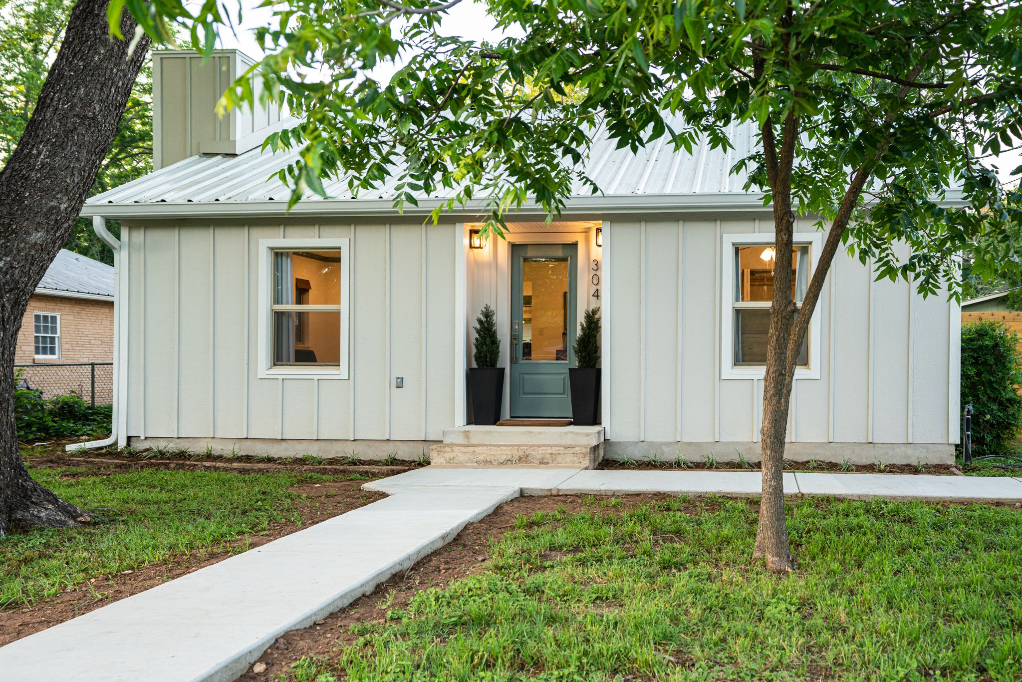 White modern farmhouse style home with vertical siding and landscaped yard viewed from multiple angles.