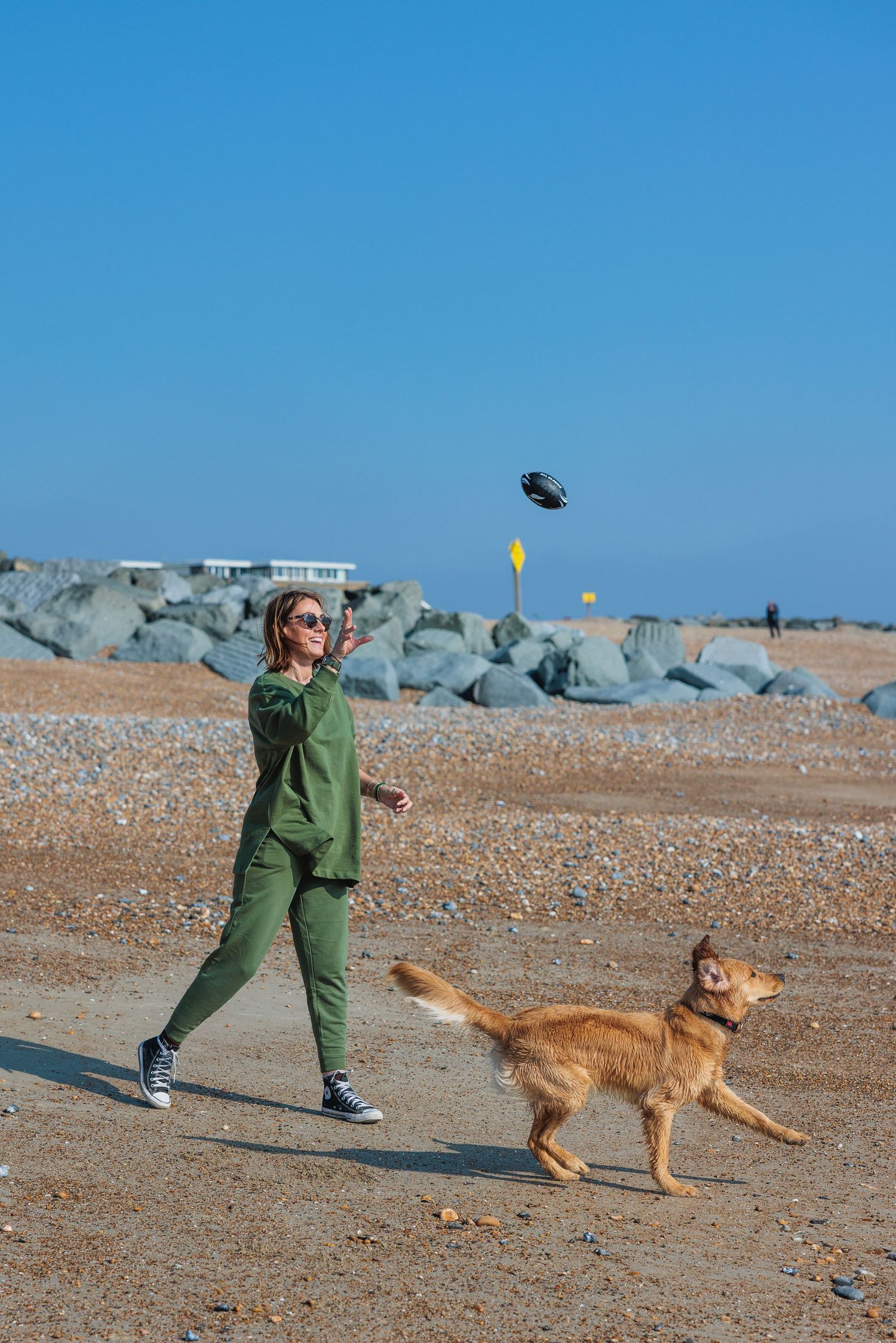 The only Girl in the house Jess throwing a ball for her dog on the beach she is wearing a green tracksuit